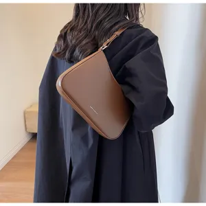 Detailed view of stylish retro brown leather shoulder baguette bag worn by model indoors.