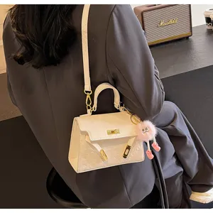Elegant white top-handle Kelly bag with cute fluffy pink charm, stylish shoulder crossbody design.