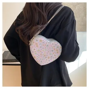 Detail view of the pink heart-shaped crossbody bag with floral pattern and silver chain.