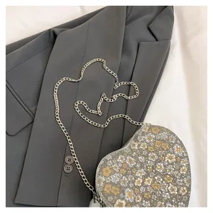 Heart-shaped floral crossbody bag detail, stylish metallic chain and chic aesthetic design.
