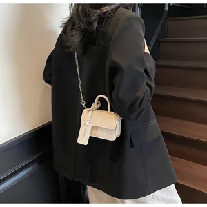 Detail view of stylish color-block mini handbag worn on shoulder with chain strap and chic tag.