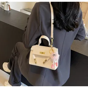 White embossed Kelly handbag detail with metal lock and pink fluffy charm pendant.