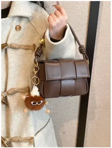Detailed view of dark brown woven leather shoulder bag with chic plush charm and metal chain.