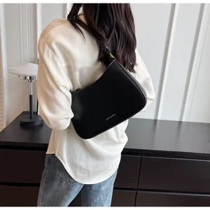 Detailed back view of a sleek black baguette shoulder bag worn with a white shirt.