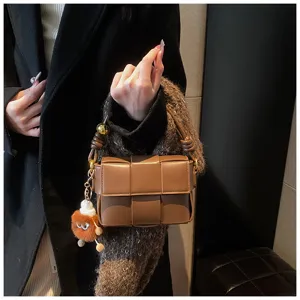 Detailed shot of a brown woven leather handbag with knot handle and cute plush charm pendant.