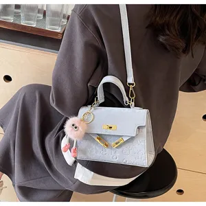 Detail view of light blue embossed Kelly style shoulder bag with cute plush furry charm pendant.