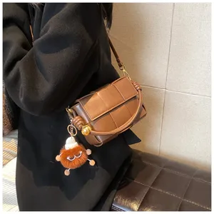 Brown woven leather shoulder bag with plush pendant, stylish winter crossbody bag for women.