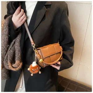 Detailed view of brown woven leather shoulder bag with chic knot handle and stylish charm.