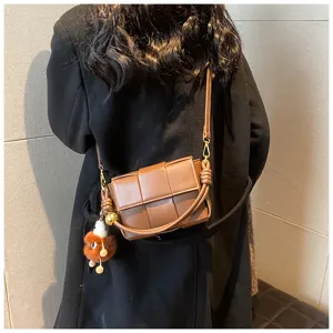 Woven leather crossbody bag for women, stylish brown shoulder bag with cute fluffy charm.