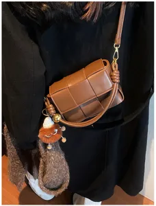 Detailed view of brown woven leather crossbody bag with knot strap and fluffy plush charm pendant.