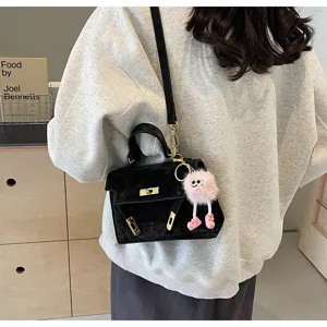 Black embossed Kelly bag detail showing metallic turn-lock clasp and cute plush charm.
