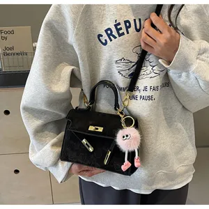 Stylish black embossed mini Kelly handbag for women with cute pink fluffy charm accessory.