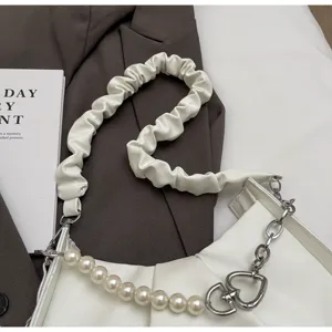 Close-up of white pleated shoulder bag featuring elegant pearl chain and heart metal link.