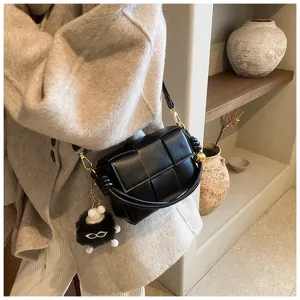Detailed shot of a black woven leather shoulder bag with chic knot design and fluffy pendant.