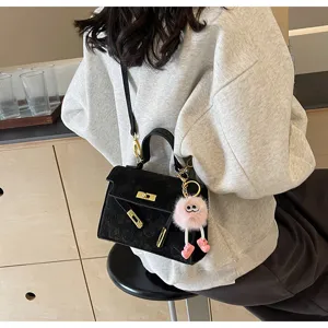 Detailed close-up shot of black embossed shoulder Kelly bag featuring a cute pink fluffy charm.