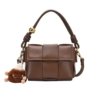 Chic woven leather shoulder bag with knotted handle and plush charm, stylish crossbody handbag.
