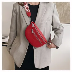 Détail d'un sac bandoulière en cuir rouge avec sangle large et zips argentés élégants.
