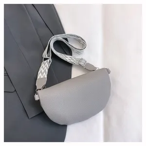Détail du sac bandoulière gris en forme de croissant avec sangle large à motifs et similicuir.