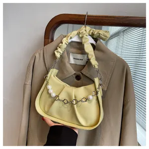 Détail de sac à bandoulière froncé jaune, chaîne en métal perlé élégante, design minimaliste.