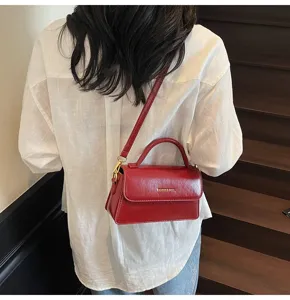 Vue détaillée du sac bandoulière rouge brillant porté, mettant en valeur la texture.