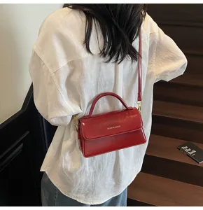 Gros plan d'un sac bandoulière élégant en cuir vernis rouge avec poignée et accessoires.