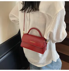 Détail de sac à bandoulière en cuir rouge montrant un design élégant et du matériel doré.