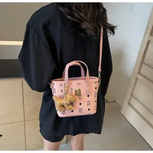 Detail shot of pink PU leather bucket bag with cute bear pendant and monogram print.