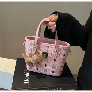 Pink leather bucket bag detail showing cute dog pendant, monogram print and metal hardware closeup.