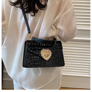 Borsa a mano nera con motivo coccodrillo, chiusura a cuore dorata e tracolla elegante.