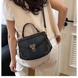 Detail shot of black studded crossbody handbag with gold lock closure and top handle.
