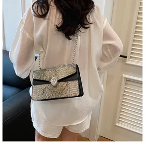 Sac à bandoulière chic avec rabat en serpent et fermoir tête d'animal pour un style élégant.