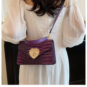 Vista dettagliata di una borsa a tracolla viola con motivo coccodrillo e chiusura a cuore.