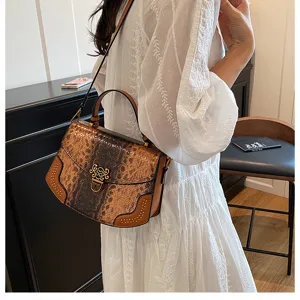 Detailed view of snake pattern shoulder bag with metal lock and rivets in indoor setting.