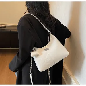 Detailed view of white patent leather shoulder bag with chic chain strap and elegant turn lock.