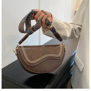 Detail view of retro brown saddle bag with stylish ethnic woven strap and metal studs.