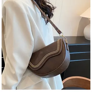 Detailed view of brown leather saddle bag with vintage curved flap and elegant shoulder strap.