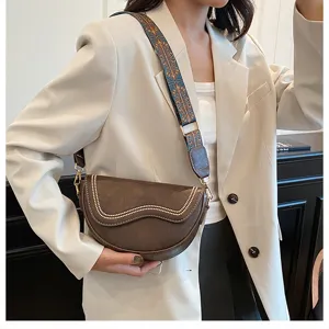 Chic brown saddle bag detail view, featuring wide patterned strap and delicate rivet accents.