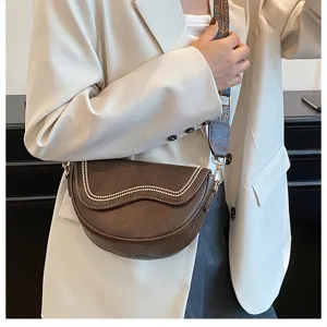 Detail view of the brown retro saddle bag featuring wavy studded flap and printed strap.