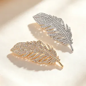 Detailed shot of glittering crystal feather brooches in gold and silver, elegant coat pins.