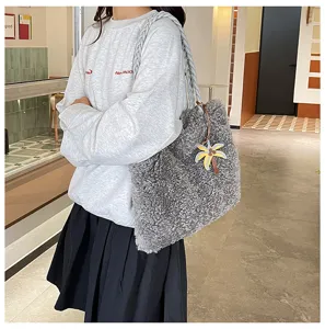 Vista de cerca del bolso tote de felpa gris con correa trenzada y colgante de palmera elegante.