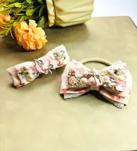 Vue détaillée d'un ensemble pince à cheveux et chouchou style lourd avec dentelle rose et strass.
