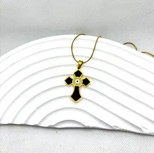 Collier croix en acier titane plaqué or avec pendentif émail noir et mauvais œil tendance.