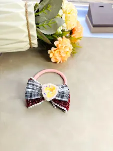 Gros plan détail d'un élastique à cheveux rose avec un nœud écossais, des perles et un strass.