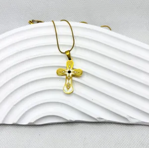 Gros plan détaillé d'un collier pendentif croix en acier titane doré avec émail blanc et strass.