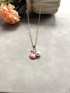 Gros plan sur le collier chaîne dorée avec un pendentif coquillage rose et perle.