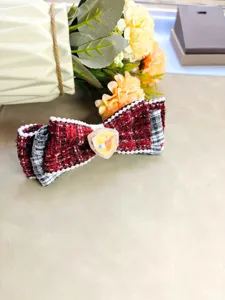 Vue détaillée de la pince à cheveux nœud en tweed rouge et noir avec perles et cristal central.