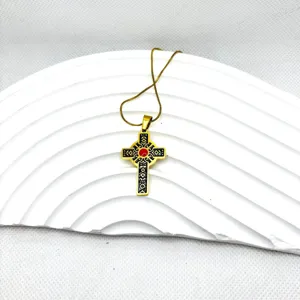 Vue rapprochée détaillée du collier avec pendentif croix en acier titane doré et pierre rouge.