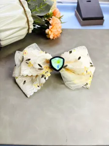Vue détaillée de la pince à cheveux nœud en dentelle douce avec centre en pierre verte.