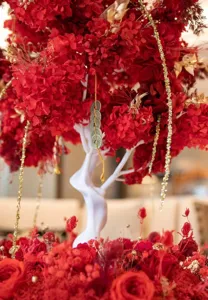 Detailed shot of red preserved hydrangea flower arrangement with white decorative tree and coins.