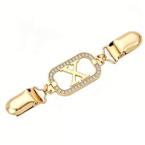 Gold tone rhinestone letter X sweater clip detail shot, elegant cardigan collar cinch brooch.